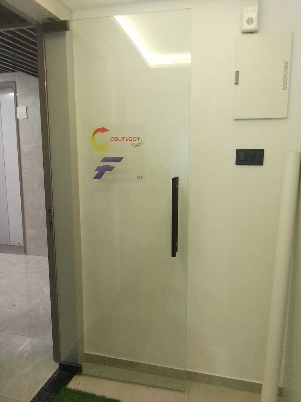 Wide view of a frosted glass office entrance door with company logo decal, lift lobby visible to the left