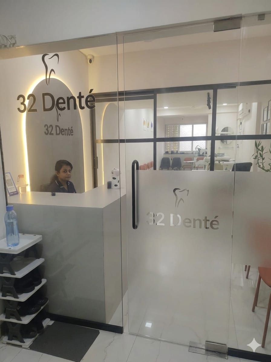 Dental clinic reception seen through a glass partition with a frosted lower panel carrying a metallic-look clinic logo