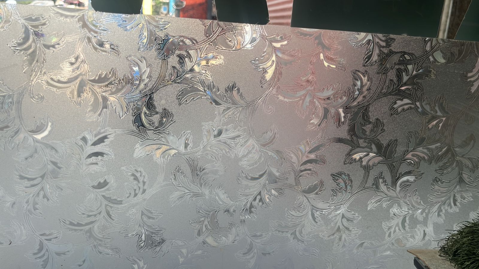 Close view of decorative window film with an etched baroque leaf and scroll pattern catching daylight