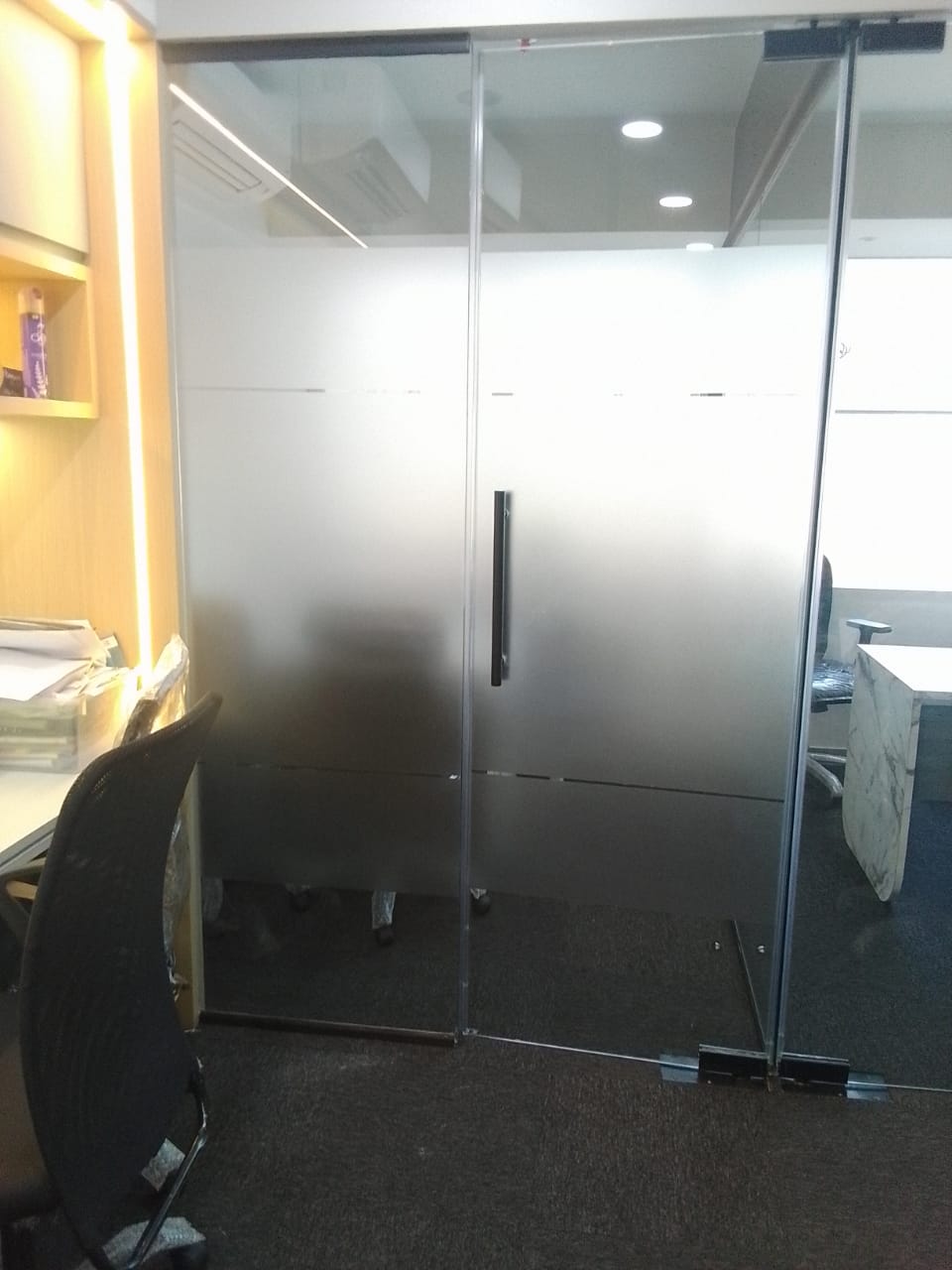 Frosted glass cabin partition and door with clear horizontal vision strips, office desks visible on either side