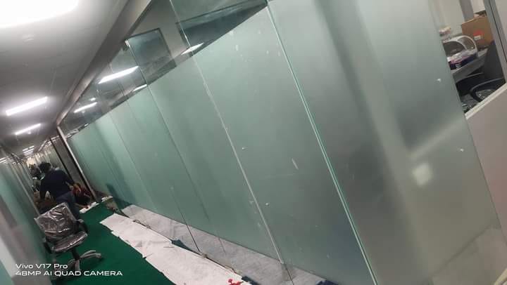 Long run of frosted film on full-height glass partitions along a commercial office corridor, protective sheeting on the floor