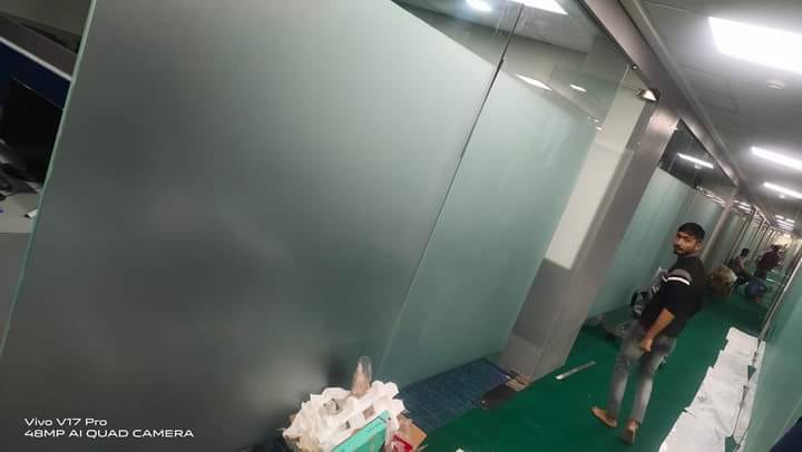Frosted glass partition beside an office corridor with a worker walking past and packing material on the floor