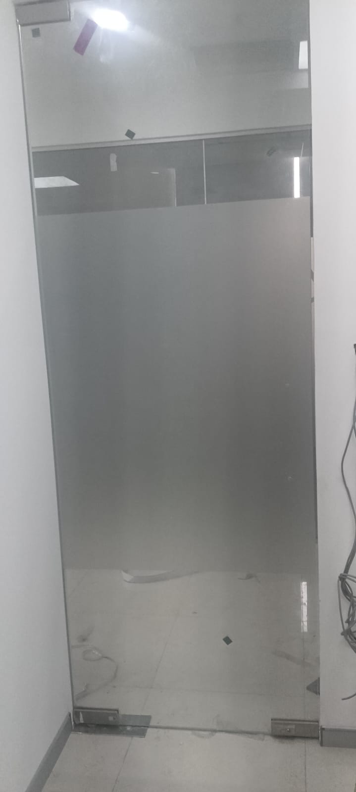 Full-height frameless glass door finished in frosted film, mounted on floor-spring patch fittings in an office lobby