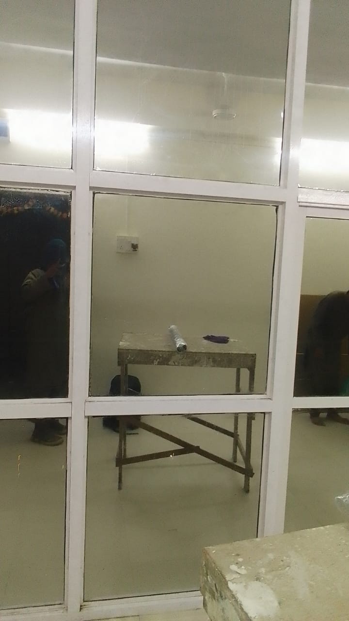 Frosted panes in a white grid partition seen from a work area, trestle table and installer visible beyond