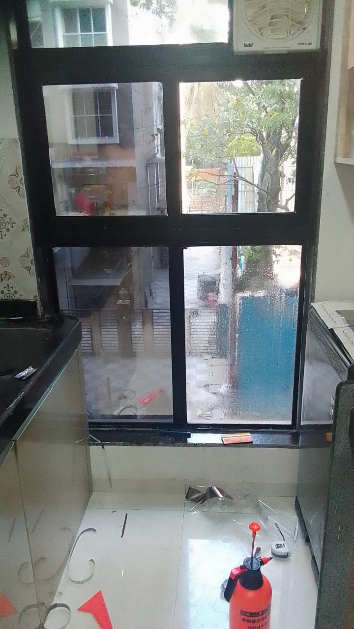 Kitchen window glass wet with application solution during film installation, film offcuts and a pressure sprayer on the floor