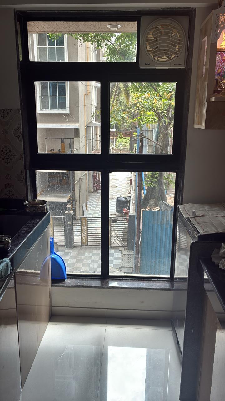 Untreated black-framed kitchen window overlooking a neighbouring building and lane before window film is applied