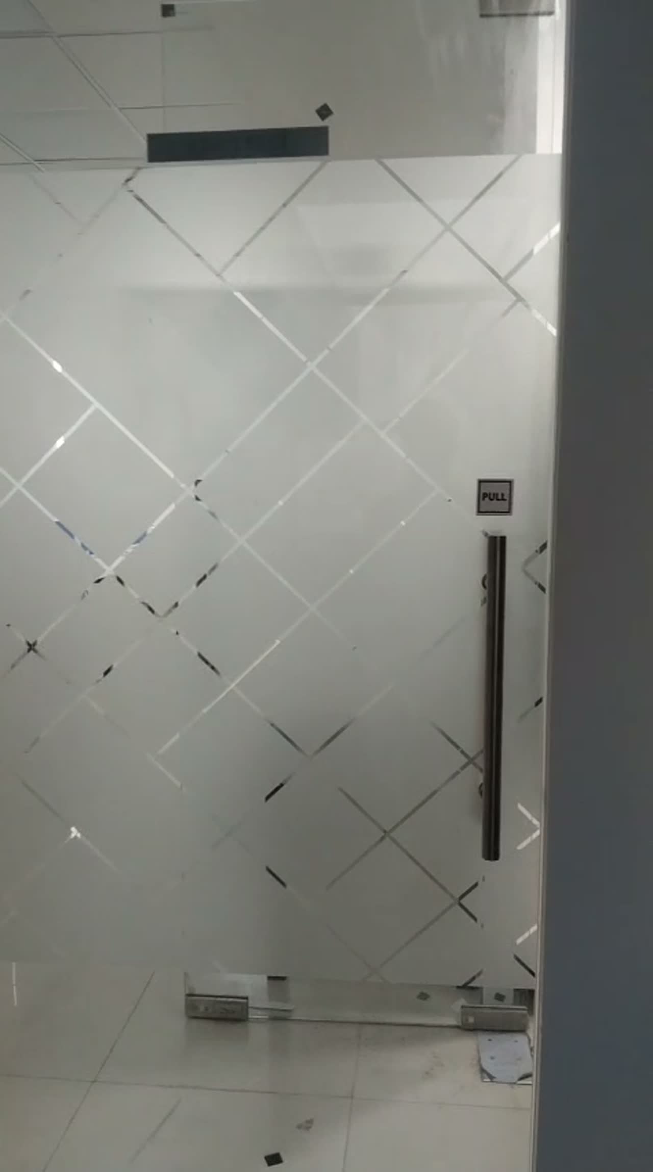 Frameless frosted glass door with diamond lattice film on floor-spring fittings in a newly finished office