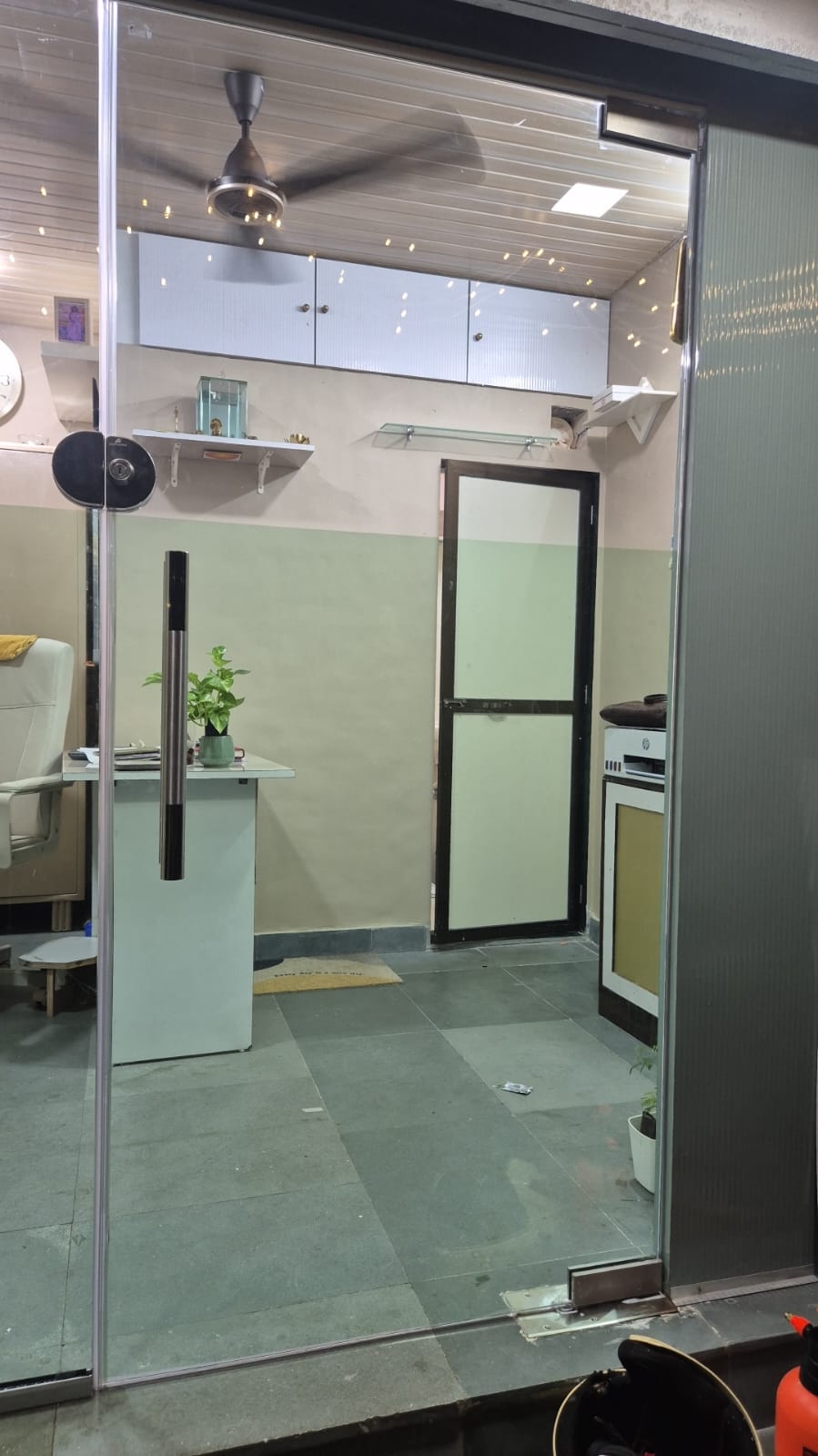 Frameless glass entrance door of a ground-floor office, with a frosted-glass internal door and reception desk visible inside