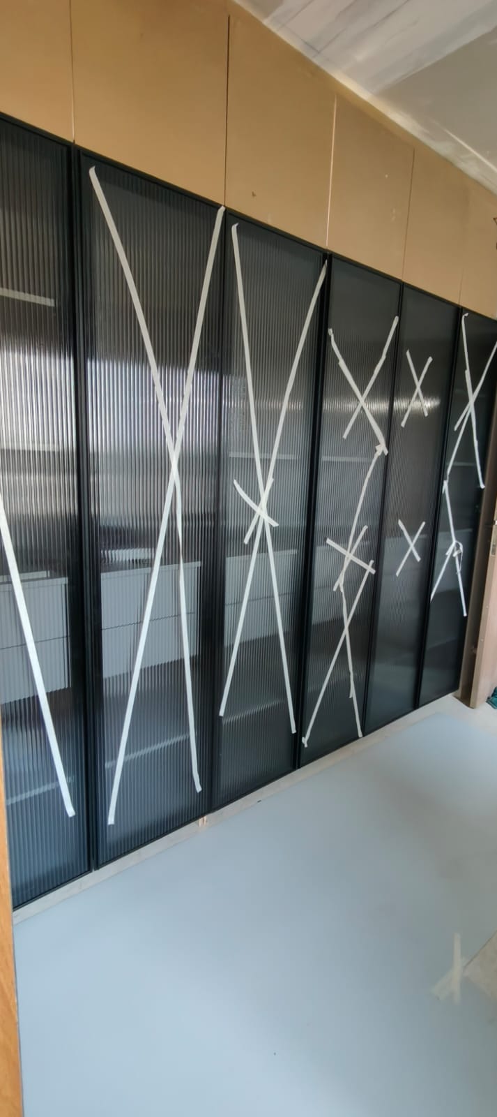 Row of black-framed reeded glass partition panels marked with protective white tape crosses on a fit-out site