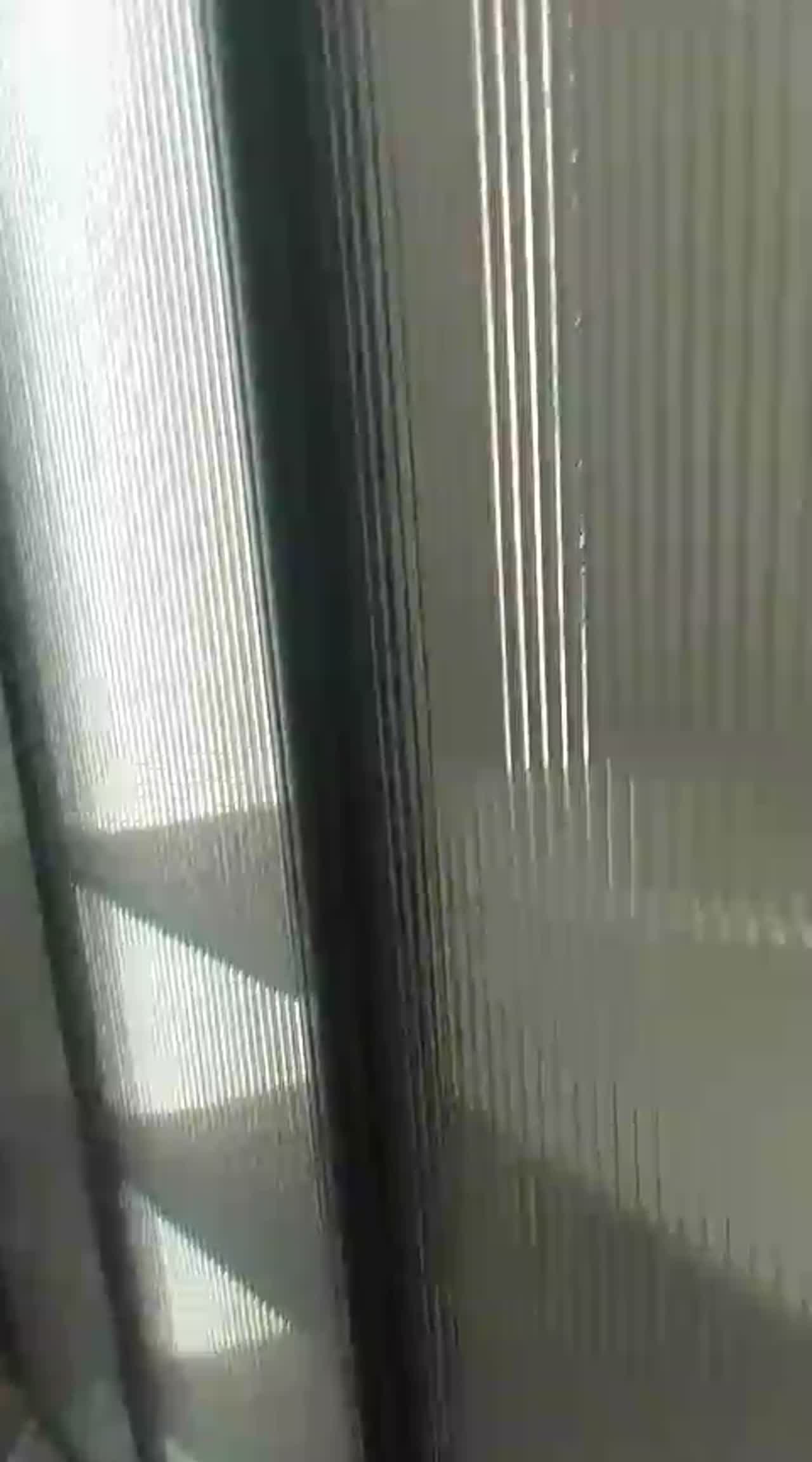 Video detail of sunlight raking across reeded film on a framed glass partition, casting striped shadows