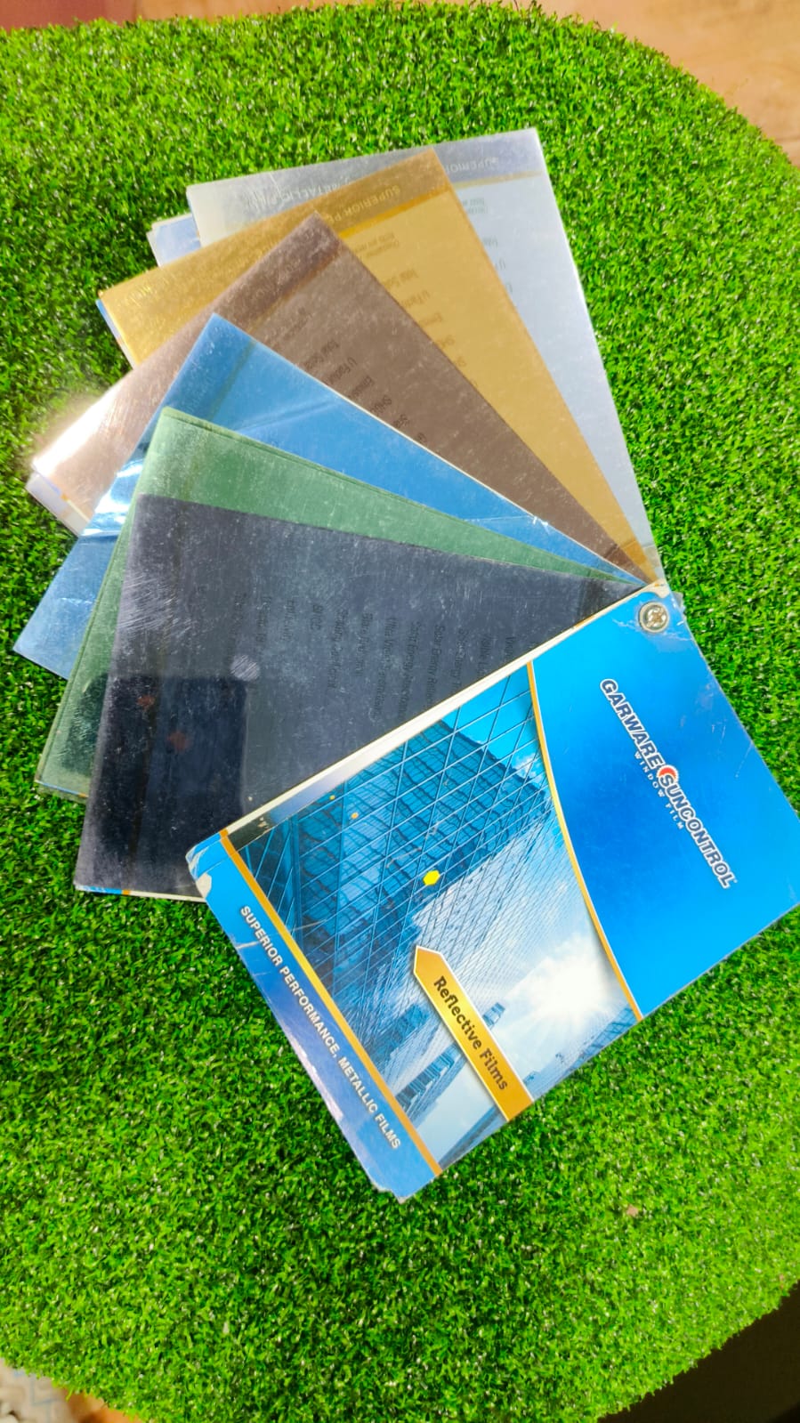 Fanned set of reflective solar film swatches in bronze, gold, blue, green, silver and charcoal beside their catalogue