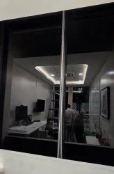 Dark tinted office window viewed at night from outside, with the lit interior and desks visible through the glass