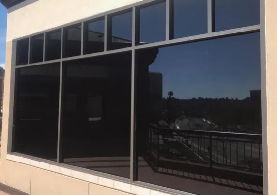 Commercial storefront glazing finished in dark reflective solar film, mirroring the sky and street under bright sun